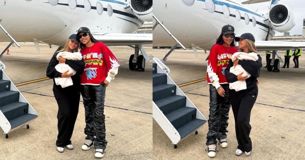 Ludmilla e Brunna Gonçalves chegam ao Brasil com a filha recém-nascida; veja Ludmilla e Brunna Gonçalves juntas, elas são duas mulheres adultas e posam juntas em pista de aeroporto, ao lado da escada de um jato particular branco. Uma delas segura um bebê enrolado em manta clara, enquanto a outra usa moletom vermelho, calça escura e boné. Ambas vestem roupas casuais e tênis, trocando olhares e sorrisos em um dos registros. Ao fundo, aparecem a aeronave, o concreto da pista e funcionários do aeroporto ao longe.