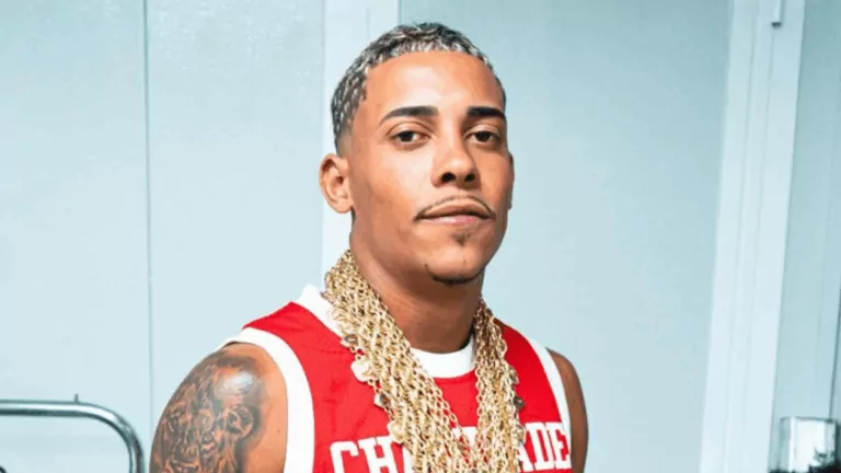 MC Poze do Rodo em retrato com camisa vermelha e correntes douradas, posando diante de parede clara.