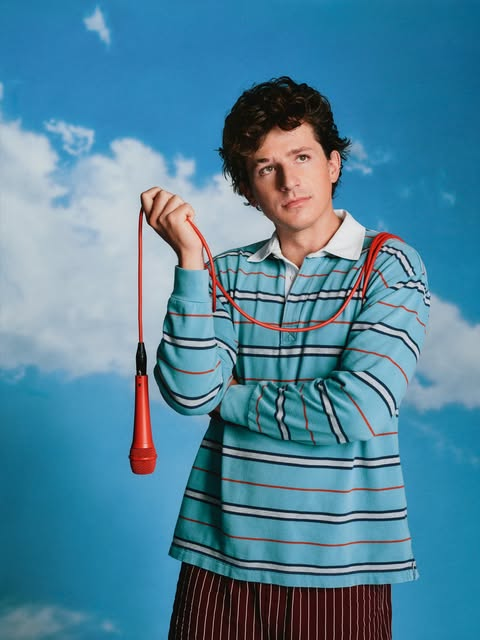 Charlie Puth posa com microfone vermelho em frente a um fundo azul com nuvens, em imagem promocional da nova fase da carreira