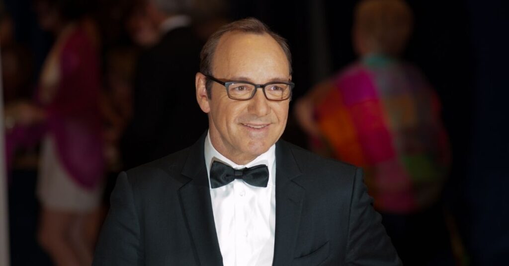 Kevin Spacey sorri em evento de gala, usando smoking preto e óculos