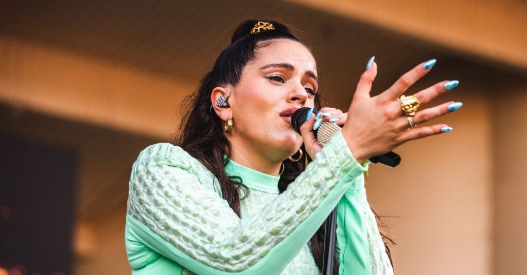 Rosalía canta em apresentação ao vivo usando look verde claro e segurando microfone