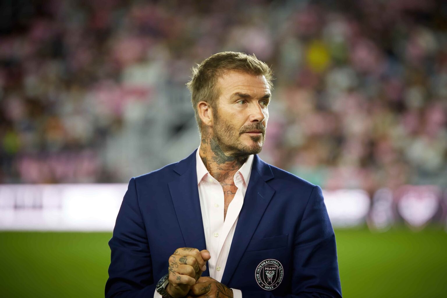 David Beckham durante evento esportivo, usando paletó azul com o brasão do Inter Miami CF.