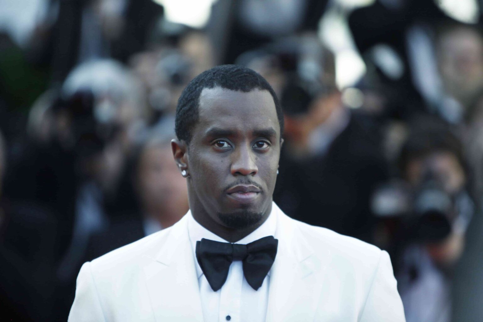 Sean “Diddy” Combs posa de terno branco e gravata borboleta em evento, antes de cumprir pena em prisão nos Estados Unidos.
