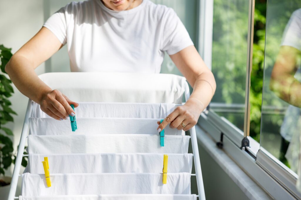 O truque caseiro que devolve o branco da roupa e elimina manchas sem esforço 1 Mulher estendendo roupa branca no varal após usar a mistura caseira para limpar roupa branca e remover manchas.