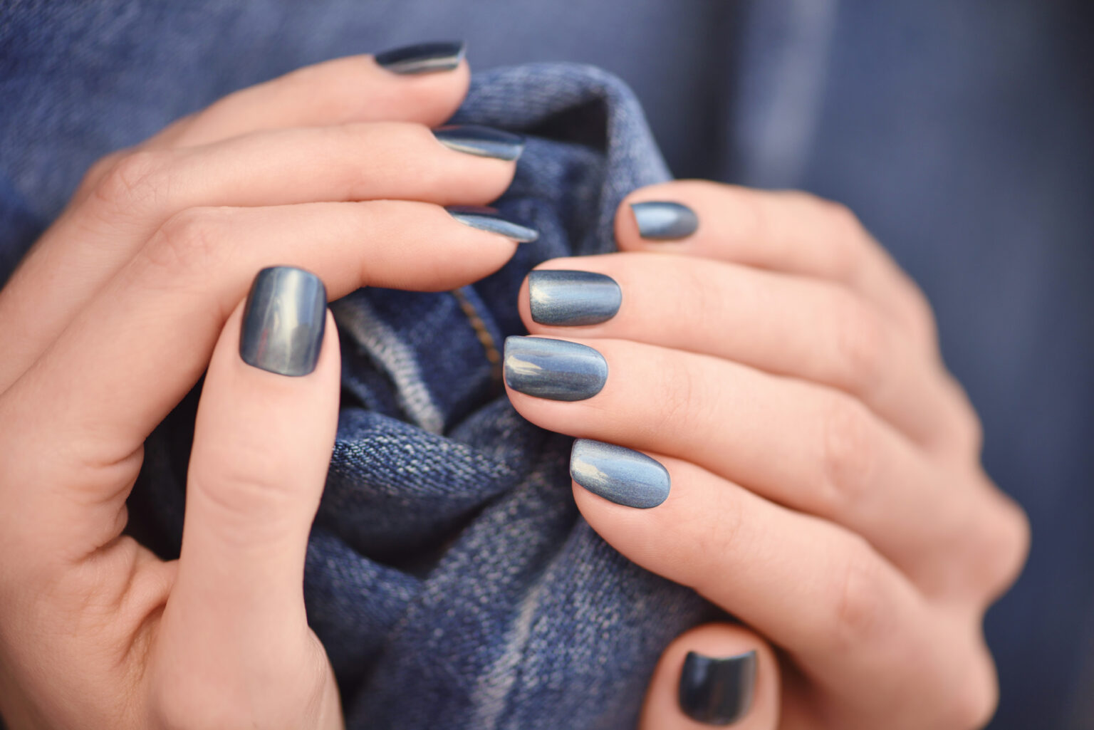 Mãos com esmalte azul-marinho destacando unhas bem feitas, representando uma das cores de esmalte que transmitem poder e confiança.