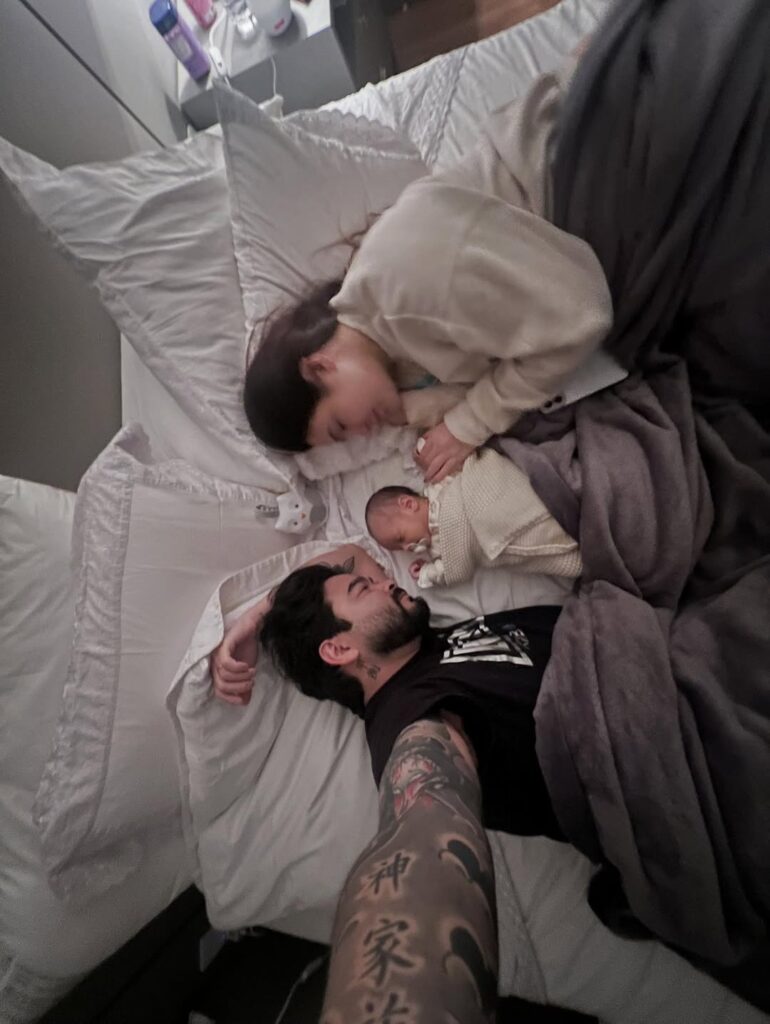 Chegadas que emocionaram: relembre os bebês de famosos que nasceram em 2025 7 Yudi Tamashiro e mulher descansa na cama ao lado do bebê recém-nascido, em foto registrada em casa.
