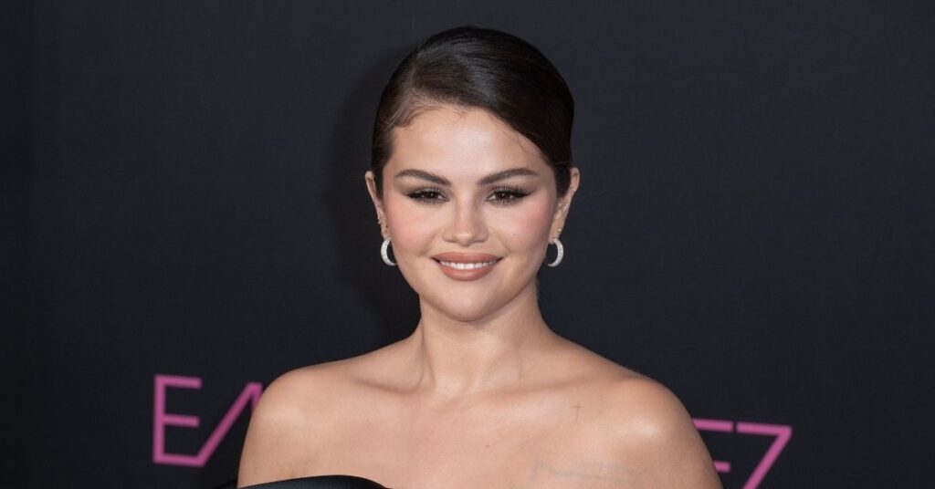 Selena Gomez explica mudança na voz e tranquiliza fãs durante live; assista Selena Gomez posa para fotos em evento oficial, usando vestido preto tomara que caia e cabelos presos, diante de fundo escuro com iluminação profissional.