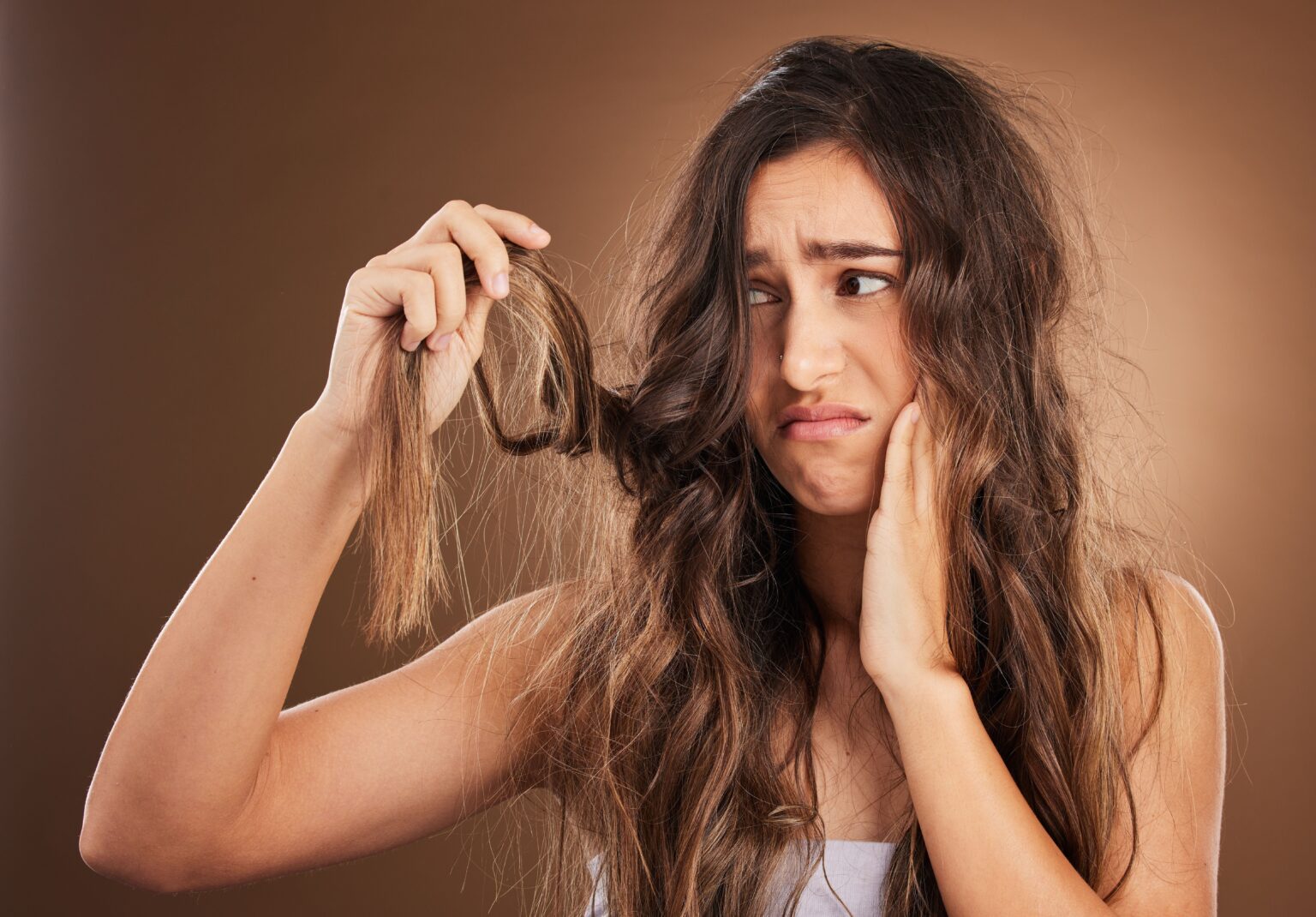 Cabelo fraco e quebradiço? 7 hábitos que devolvem força e resistência aos fios mulher observa cabelo fraco e quebradiço nas mãos, ilustrando danos capilares e a necessidade de cuidados para recuperar força e resistência dos fios