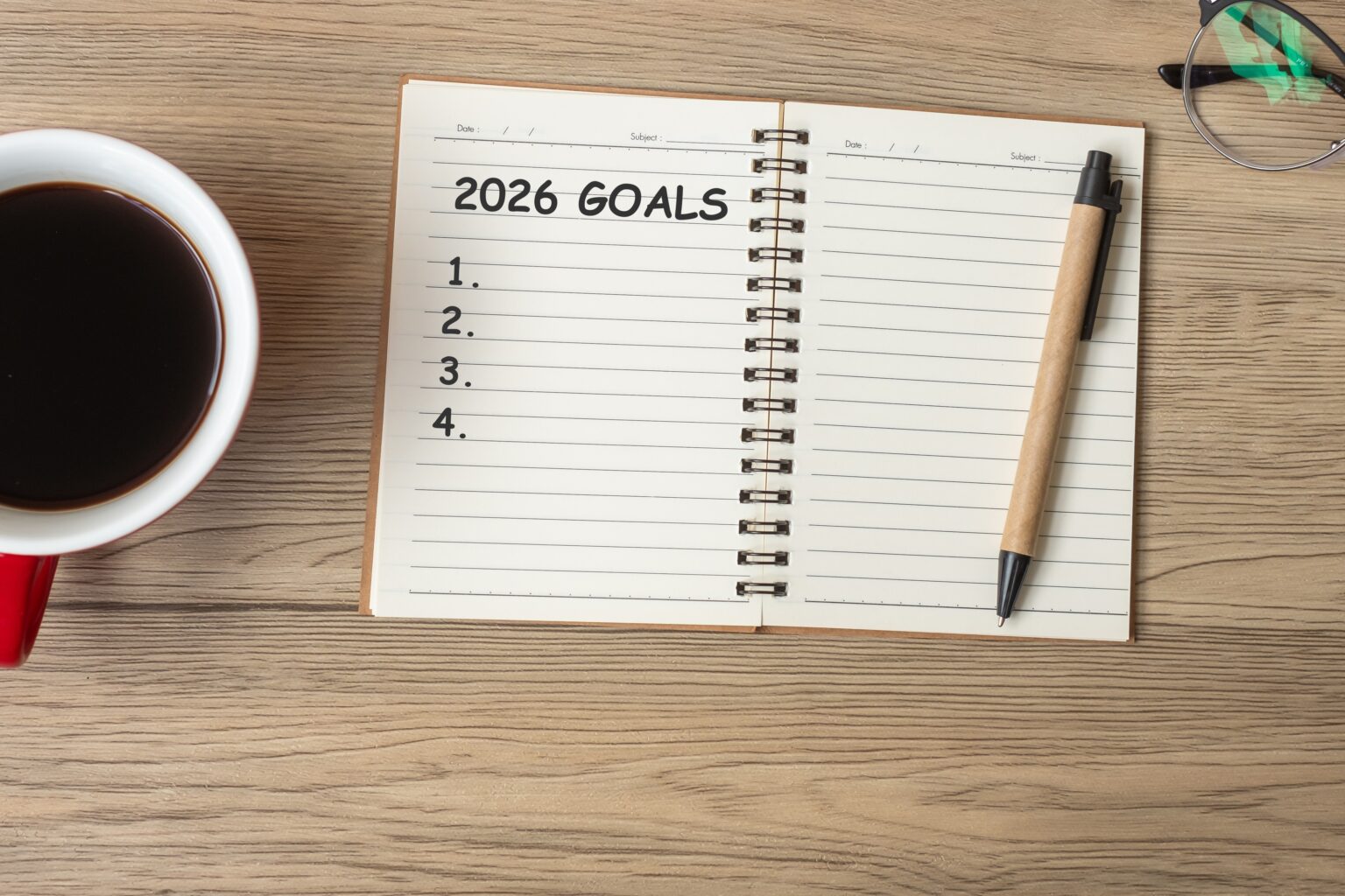 Ano novo, vida nova: 11 estratégias práticas para tirar as resoluções do papel Caderno aberto com o título “2026 goals”, lista de metas numeradas, caneta ao lado e xícara de café, simbolizando resoluções de Ano Novo e planejamento pessoal.