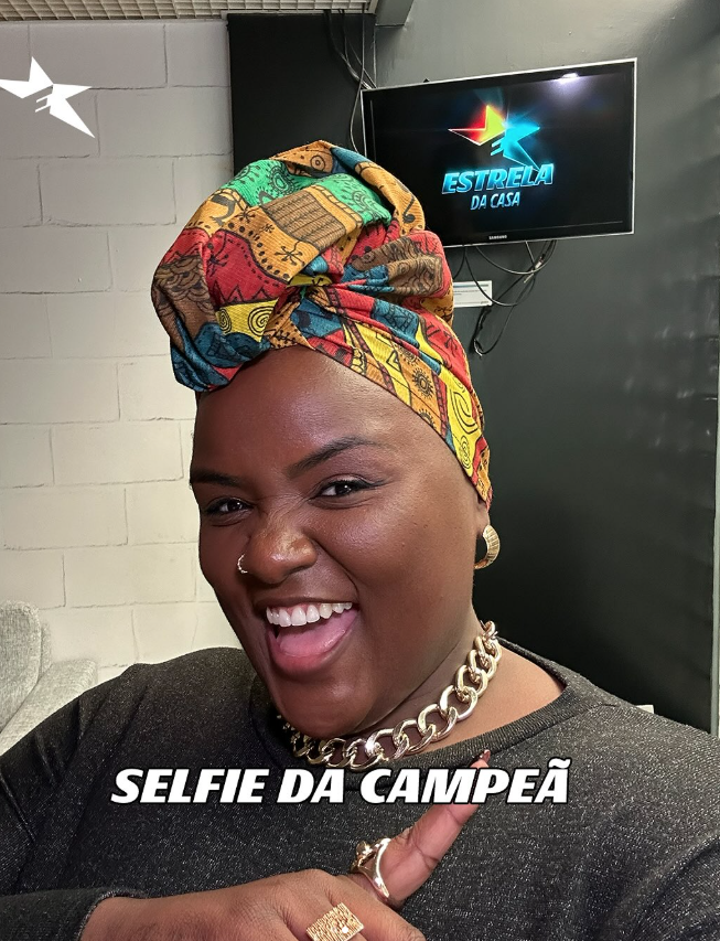 Quem venceu os realities em 2025? Relembre os campeões do ano na TV 2 Thaina Gonçalves sorri em selfie nos bastidores do programa Estrela da Casa, usando turbante colorido e exibindo gesto de comemoração após vitória.