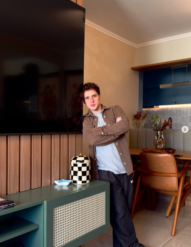 Quem venceu os realities em 2025? Relembre os campeões do ano na TV 6 Diego Martins posa em ambiente residencial moderno, encostado em móvel da sala com braços cruzados, em registro casual que destaca o estilo e o espaço decorado.
