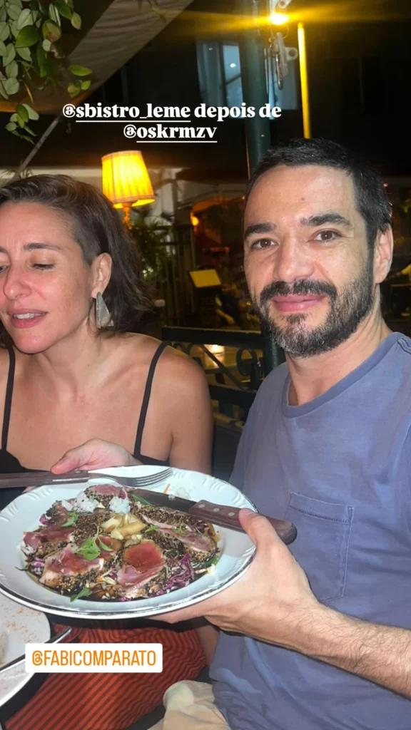 Caio Blat inicia novo romance; saiba quem é a namorada do ator 1 Caio Blat posa sorridente ao lado de Fabiana Comparato durante jantar em restaurante, segurando um prato de comida, em registro compartilhado nas redes sociais.