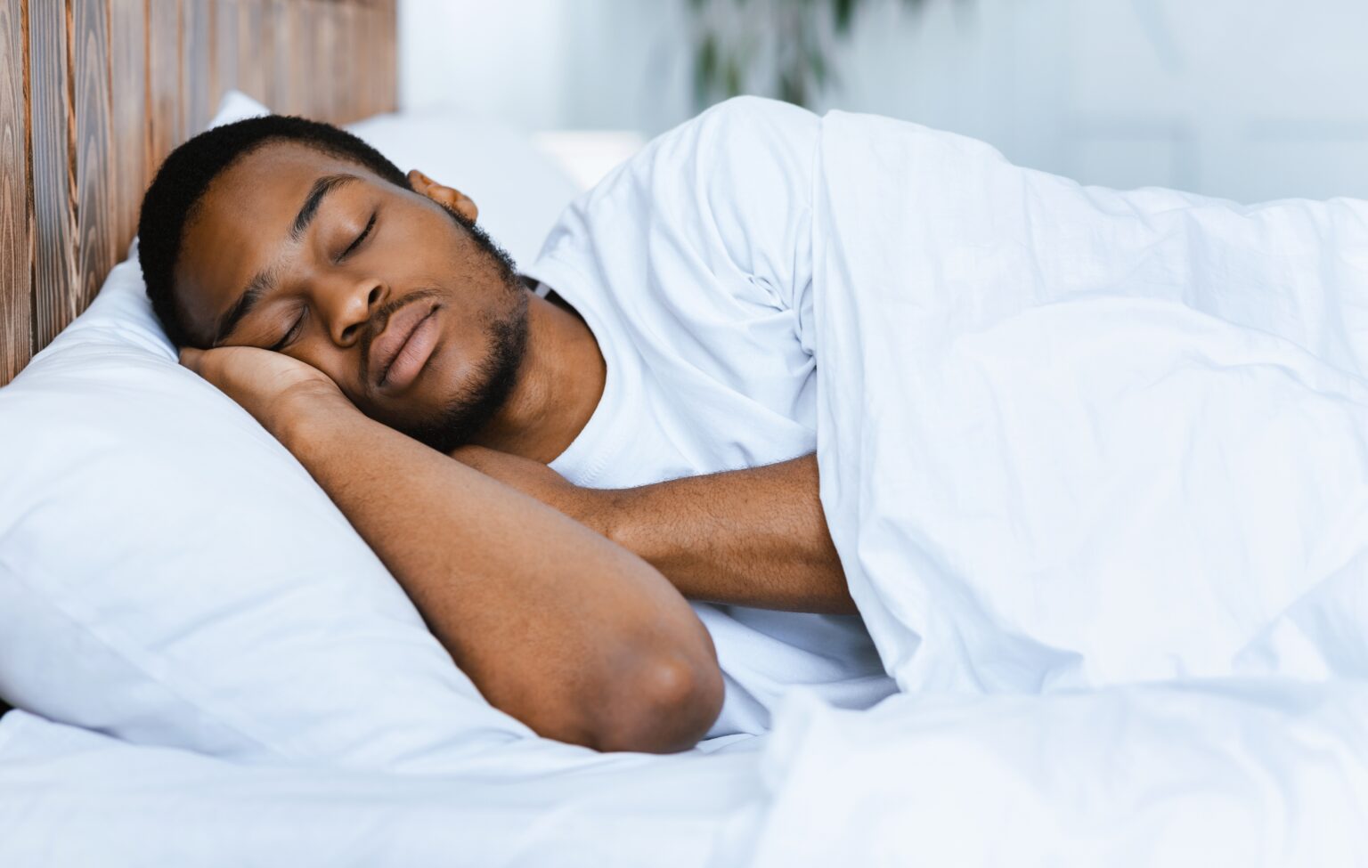 Homem dormindo de lado em cama branca, imagem que ilustra a paralisia do sono, seus sintomas e formas de prevenção