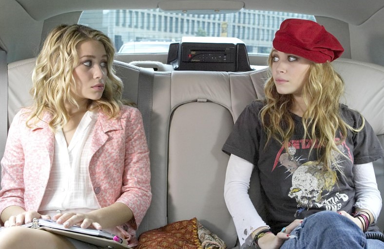 Ashley e Mary-Kate Olsen em cena do filme No Pique de Nova York, sentadas no banco traseiro de um carro e trocando olhares, imagem que relembra a fase das celebridades que sumiram dos holofotes após o auge.