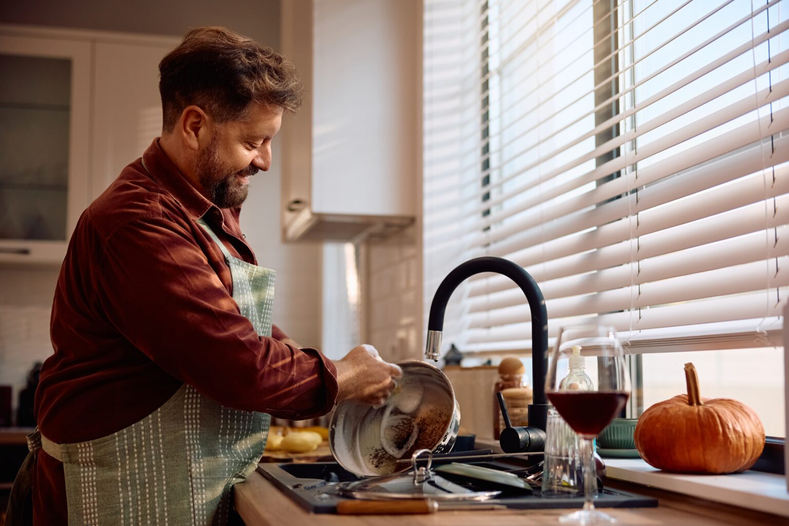 Homem lavando panela na pia da cozinha, imagem ilustrativa sobre como eliminar mau cheiro na pia e no ralo da cozinha com limpeza correta do encanamento.