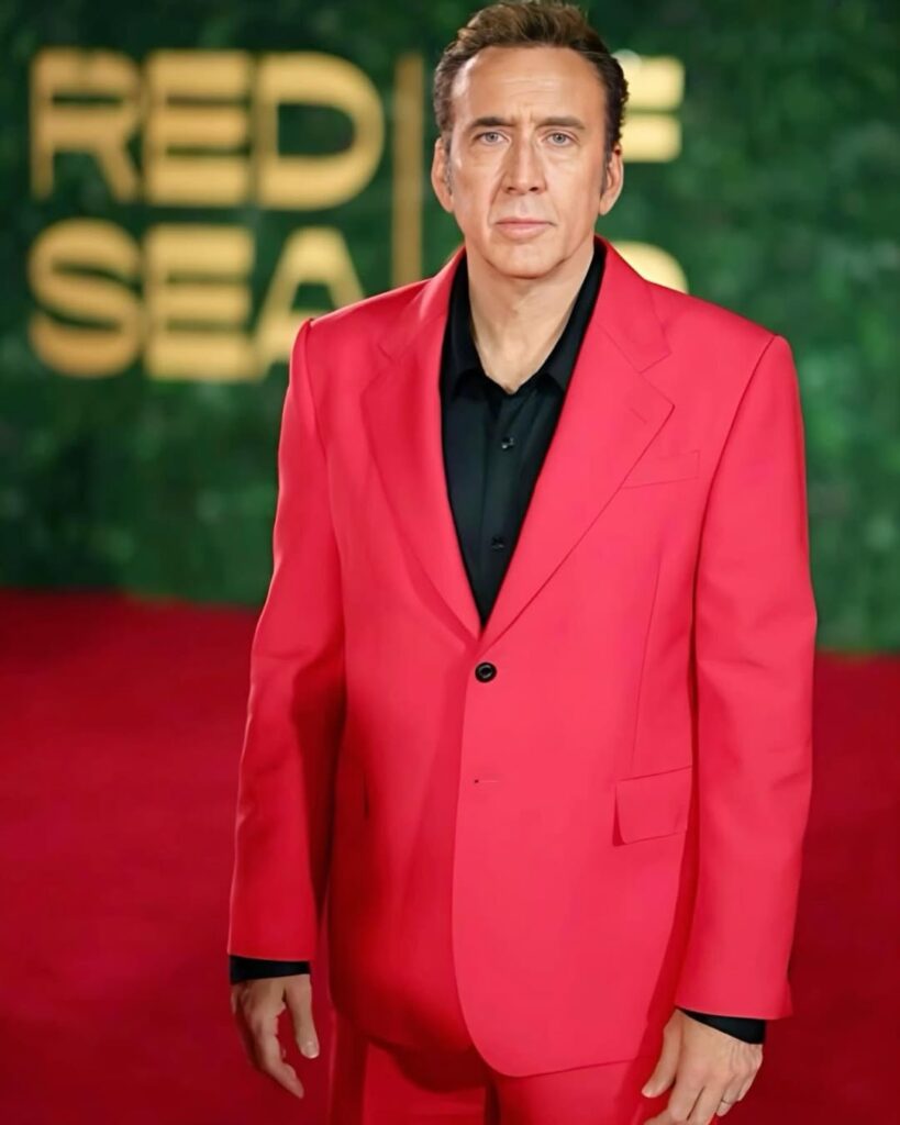 Famosos que perderam tudo: 10 celebridades que enfrentaram crises financeiras e deram a volta por cima 2 Nicolas Cage de terno vermelho em evento representando famosos que perderam tudo