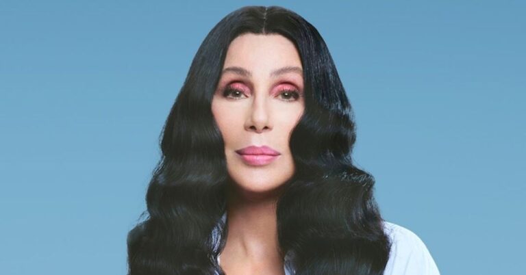 Cantora Cher em retrato oficial com fundo azul, usando maquiagem rosa e cabelo longo preto ondulado; filho foi preso nos EUA