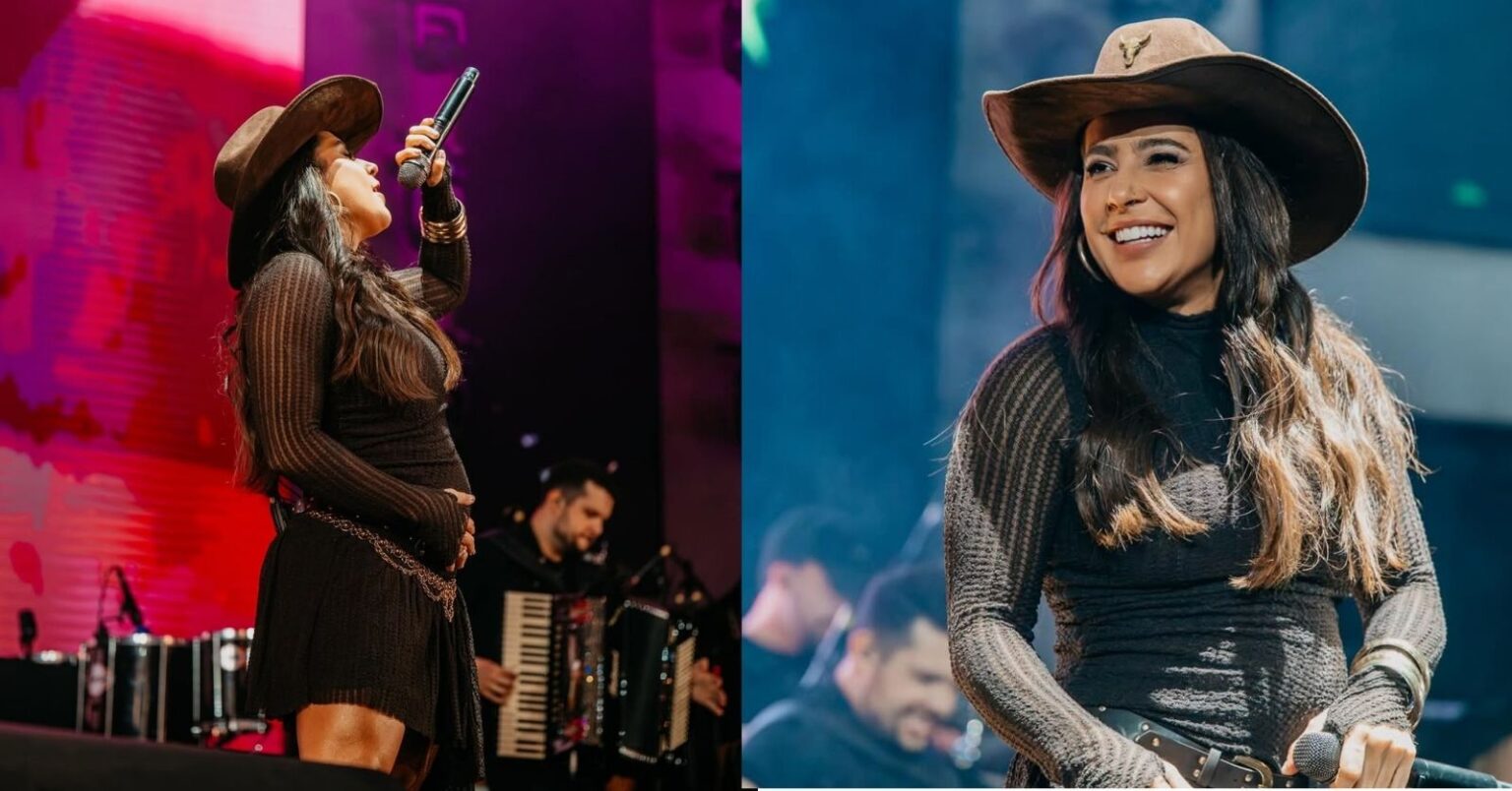 Lauana Prado surge com barrigão à mostra durante apresentação no palco, usando chapéu e segurando microfone em show.