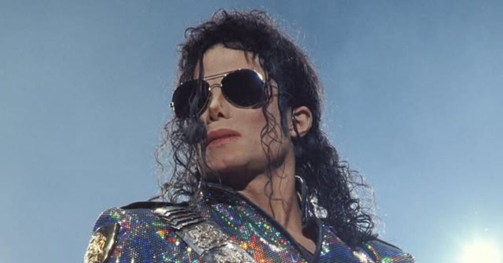 Michael Jackson com óculos escuros e jaqueta brilhante durante apresentação em palco.