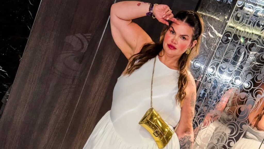 Thais Carla posa em ambiente interno usando vestido branco e bolsa dourada, exibindo look em foto compartilhada nas redes sociais.