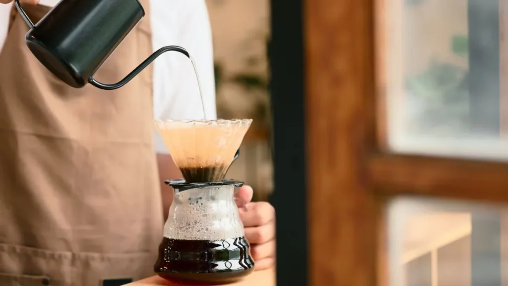 Café coado perfeito: 3 truques simples que fazem toda a diferença Pessoa preparando café coado com filtro de papel e chaleira de bico fino, mostrando técnica de preparo para um café mais equilibrado e saboroso