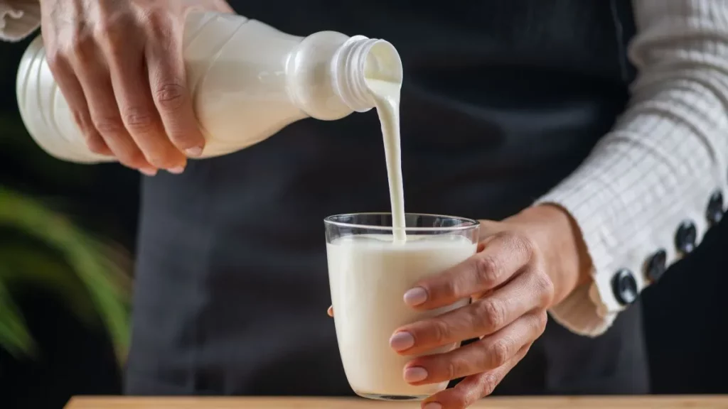pessoa servindo bebida fermentada tipo kefir em copo de vidro, alimento probiótico associado à saúde intestinal e equilíbrio digestivo