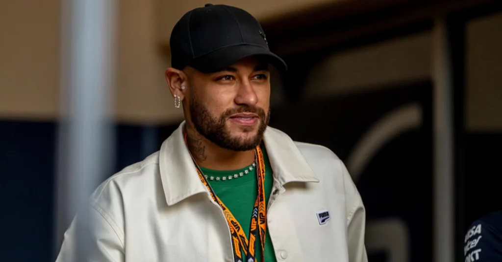 Neymar aparece de boné preto, jaqueta clara e camisa verde em ambiente interno durante evento de Fórmula 1