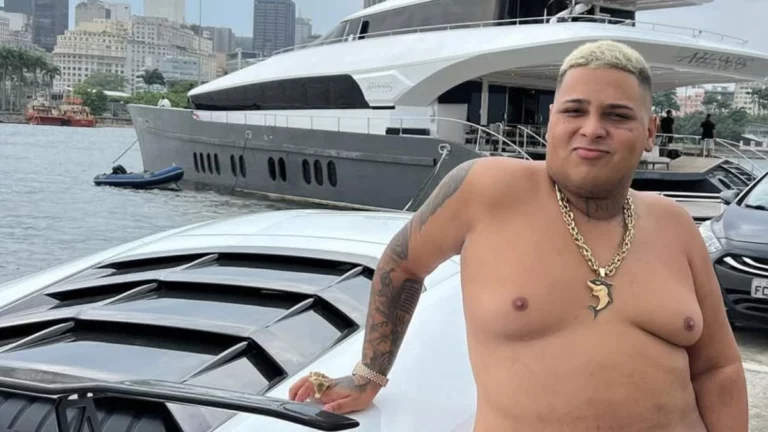 MC Ryan SP sem camisa posando ao lado de carro de luxo com iate ao fundo em área portuária