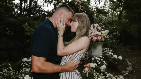 Foto de Taylor Swift e Travis Kelce abraçados em um jardim. Eles encostam as testas e Taylor acaricia o rosto de Travis.
