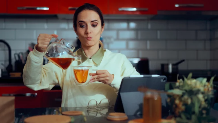 6 chás termogênicos que podem ser aliados para quem busca perder peso no inverno Mulher servindo chá termogênico em xícara na cozinha durante o inverno