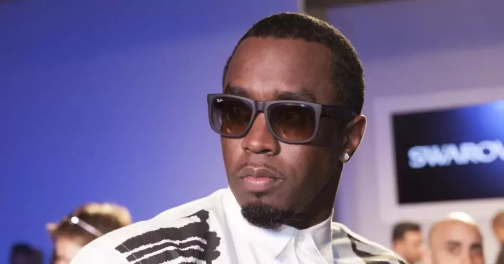 P. Diddy tem data de soltura adiantada pela 2ª vez; confira Sean Combs, conhecido como P. Diddy, usa óculos escuros e camisa branca durante evento em ambiente iluminado.