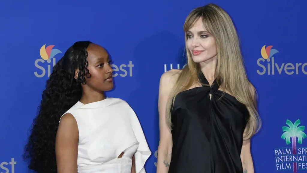 Angelina Jolie e Zahara posam juntas diante de um painel azul durante evento público.