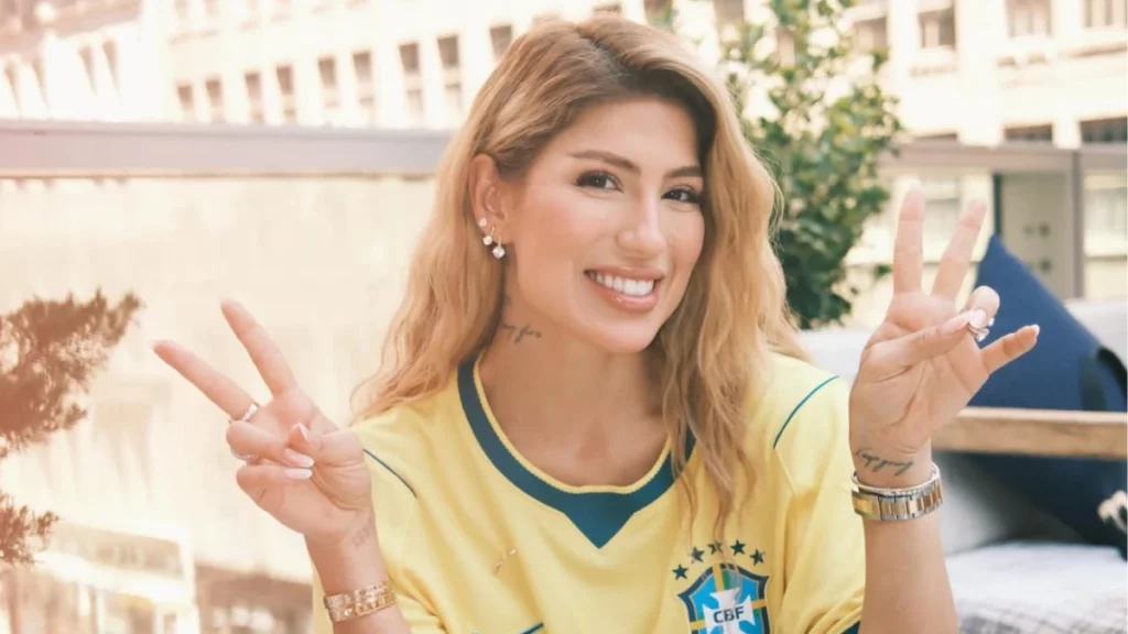 Esposa de Gabriel Magalhães, Gabi Severo abre o jogo sobre amizade entre mulheres da Seleção Gabi Severo sorri usando camisa da Seleção Brasileira enquanto faz sinal de paz com as mãos.
