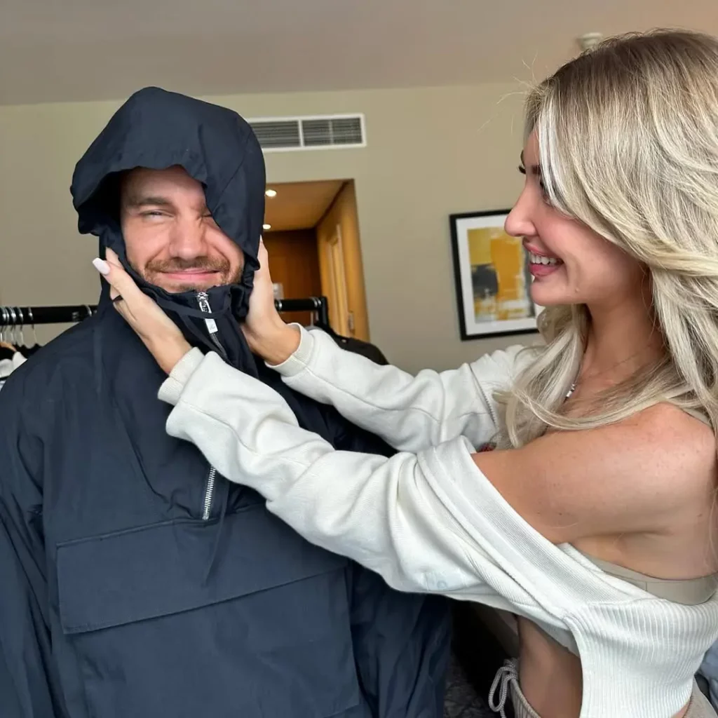 Kate Cassidy segura o rosto de Liam Payne enquanto ele veste uma jaqueta fechada até a cabeça em um quarto de hotel.