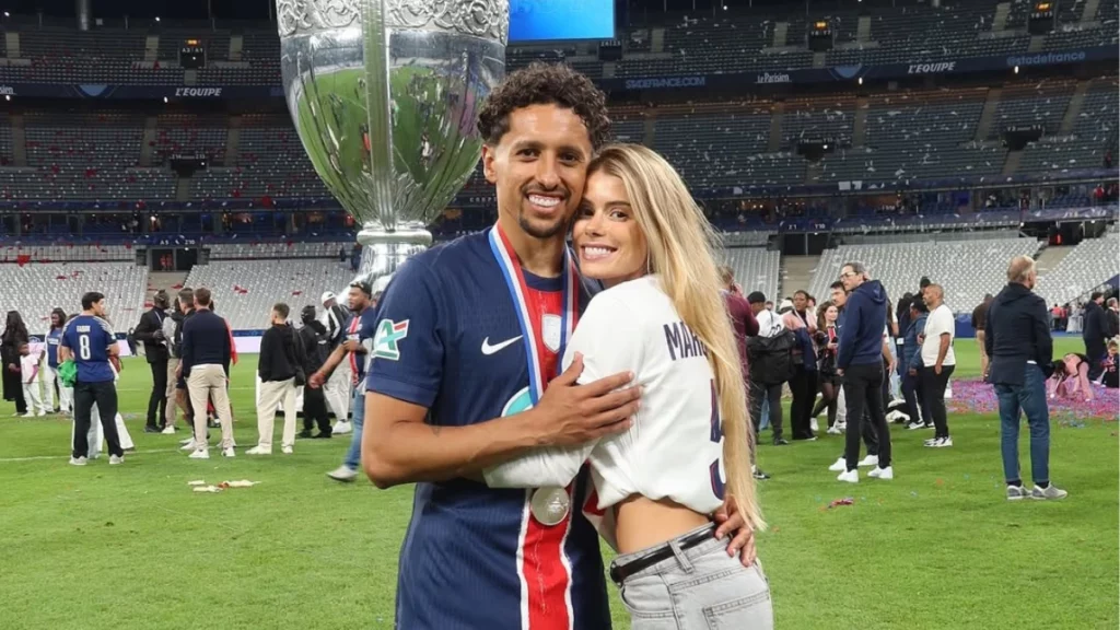 Marquinhos e Carol Cabrino posam abraçados no gramado após conquista do PSG