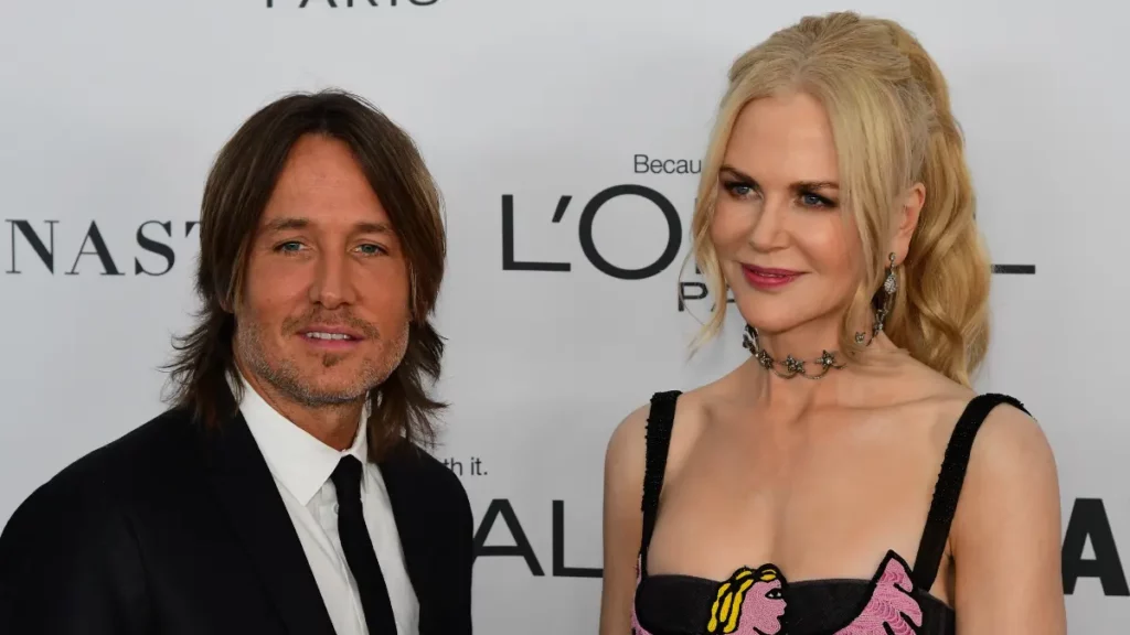 Keith Urban e Nicole Kidman posam juntos em evento de gala, olhando para os fotógrafos em frente ao painel de patrocinadores.