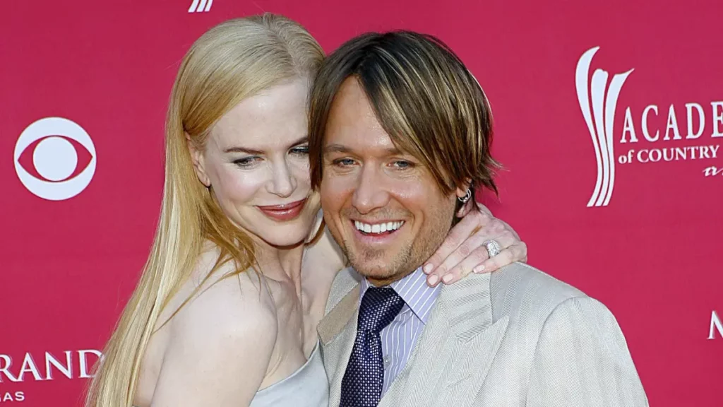 Nicole Kidman abraça Keith Urban durante evento de música country enquanto os dois sorriem para os fotógrafos.