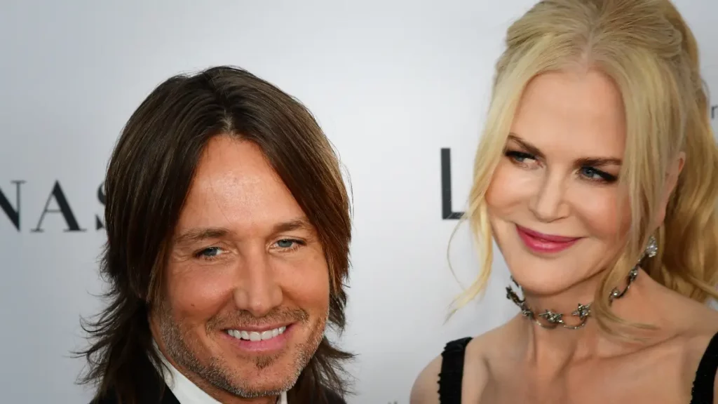 Keith Urban e Nicole Kidman posam juntos em evento de gala, olhando para os fotógrafos em frente ao painel de patrocinadores.