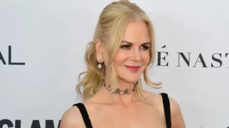 Nicole Kidman posa sorrindo em evento de tapete vermelho usando vestido preto e acessórios prateados.