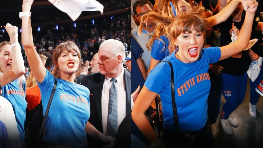 Taylor Swift comemora em meio à torcida durante partida de basquete, usando camiseta azul e levantando os braços em celebração.