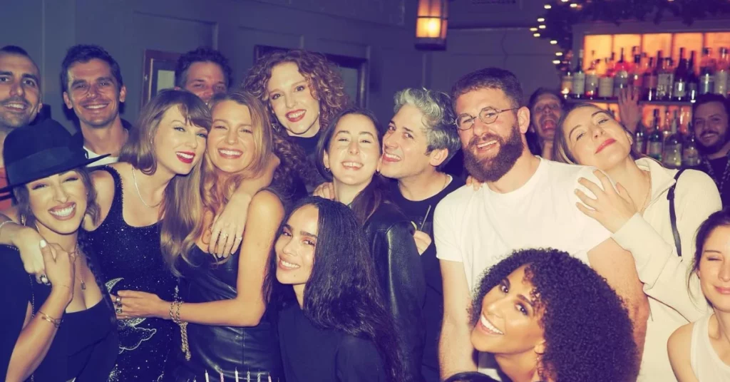 Taylor Swift aparece ao lado de Blake Lively e de um grupo de amigos em ambiente de festa, com bar iluminado ao fundo