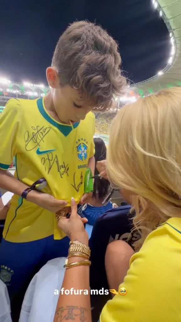 Virginia Fonseca conversa com uma criança vestindo camisa da Seleção Brasileira autografada durante jogo no Maracanã.