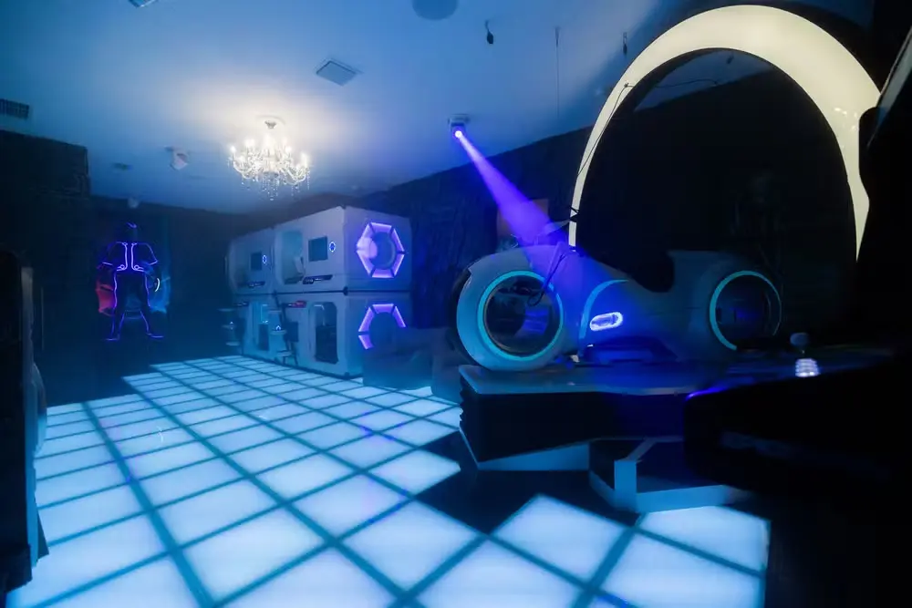 Virginia se hospeda em mansão de luxo em Orlando e valor impressiona; veja 4 Ambiente interno com piso iluminado, decoração futurista e cama em formato de veículo espacial cercada por luzes coloridas.