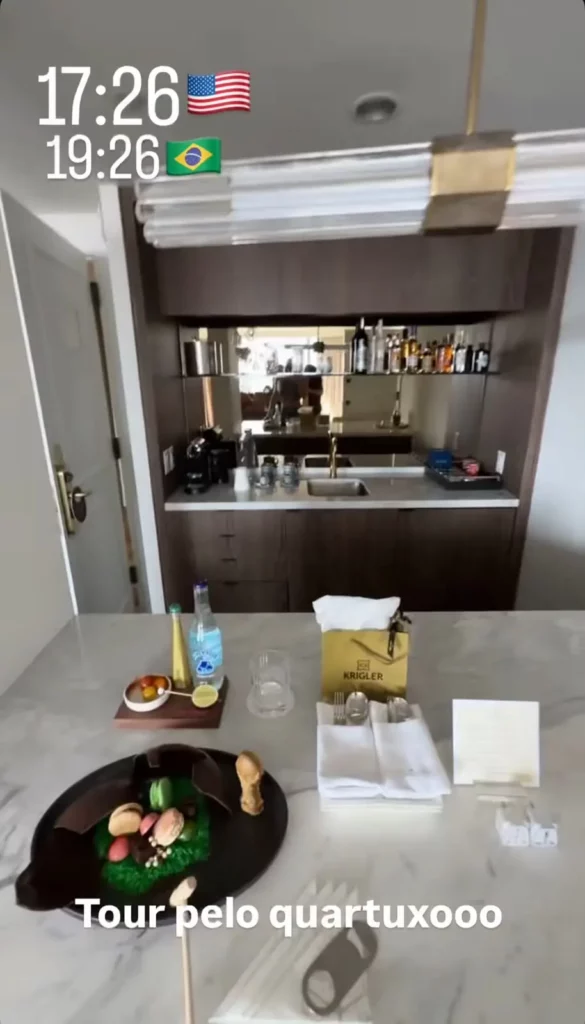 Área do minibar da suíte de Virginia com cafeteira, bebidas, frutas e doces de boas-vindas sobre a bancada.