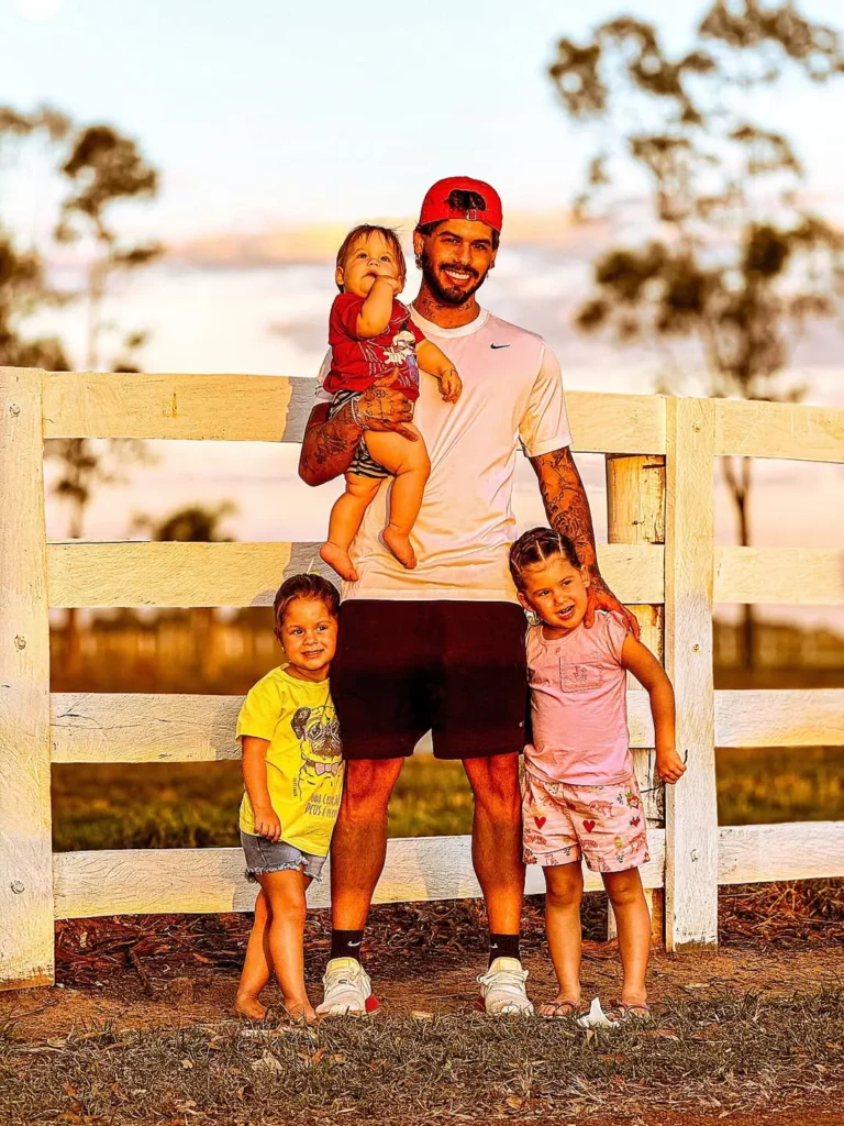 Zé Felipe posa ao ar livre com os três filhos em frente a uma cerca de madeira durante o pôr do sol.