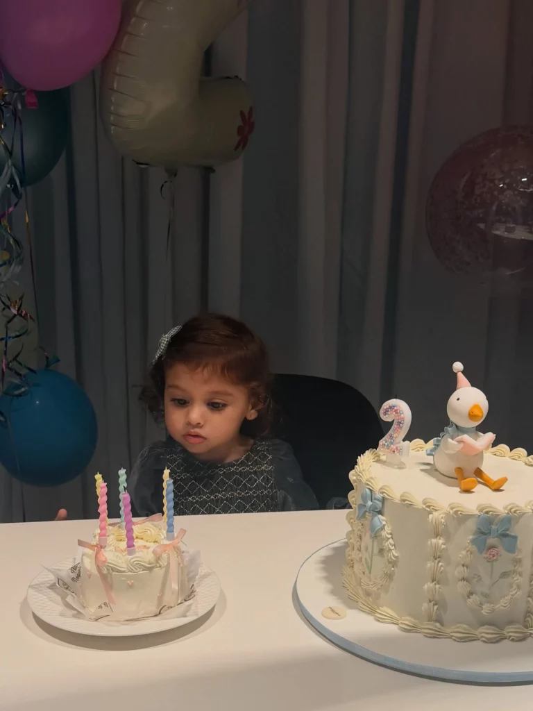 Após festa de Bruna Biancardi, Amanda Kimberlly mostra celebração intimista de Helena 1 Helena observa os bolos de sua comemoração de 2 anos, decorados em tons de branco e azul, com velas acesas e enfeite de ganso sobre o bolo principal.