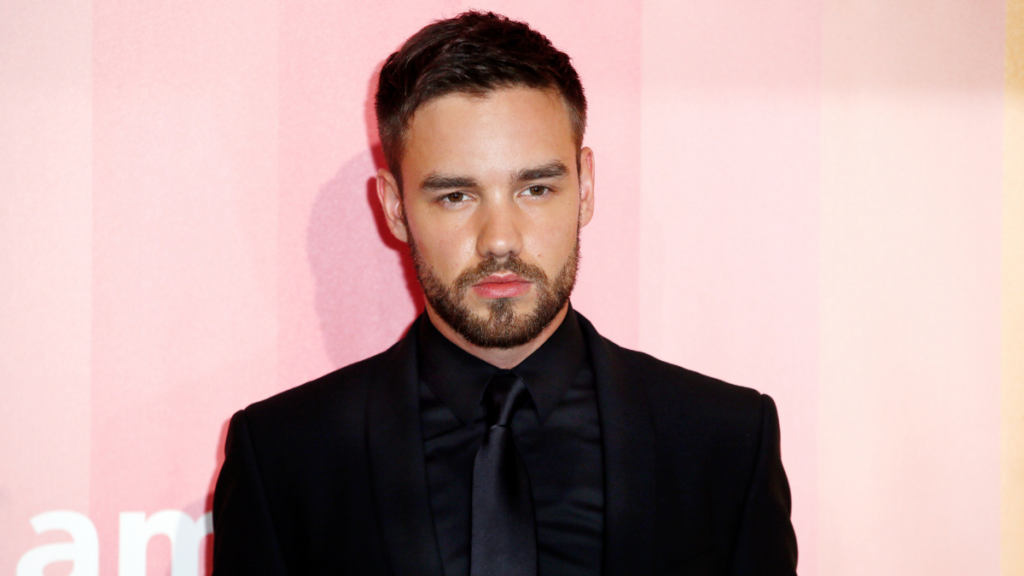 Amigo de Liam Payne é inocentado em investigação sobre morte do cantor; entenda Liam Payne posa para fotógrafos durante evento no tapete vermelho, usando terno escuro e com expressão séria para as câmeras.
