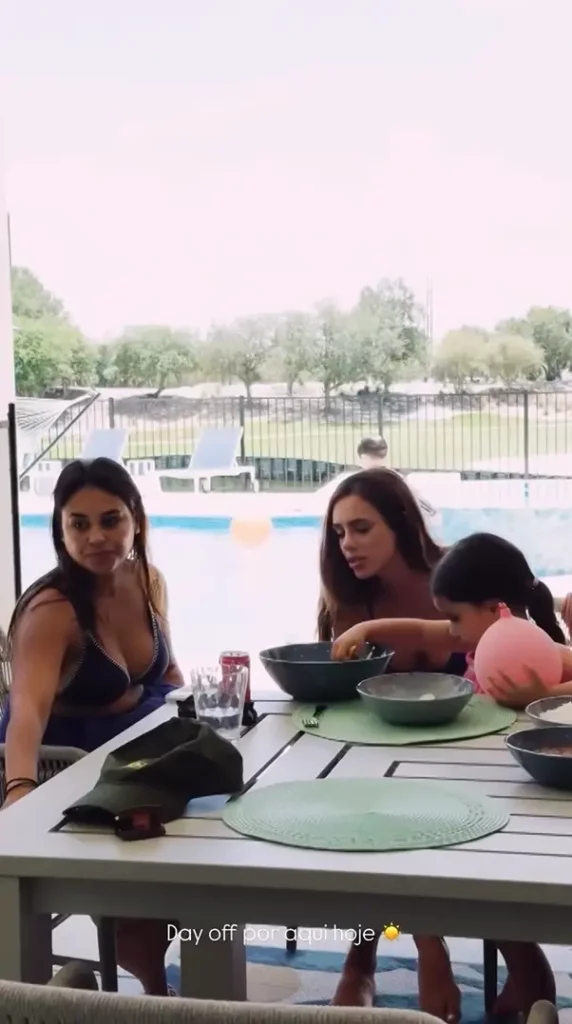 Bruna Biancardi e família ao redor de uma mesa externa durante uma refeição. Ao fundo, é possível ver uma piscina e uma área verde com árvores. Texto sobreposto: "Day off por aqui hoje ☀️".