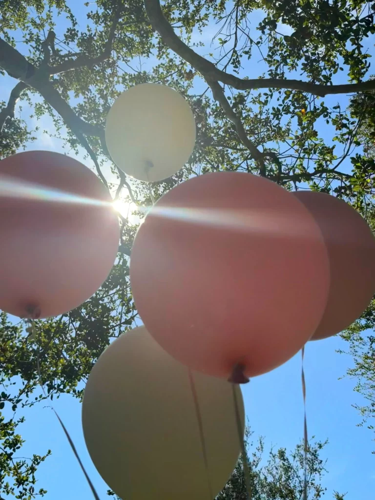 Balões nas cores rosa e branco flutuam entre as árvores durante a comemoração de aniversário ao ar livre de Gisele Bündchen.