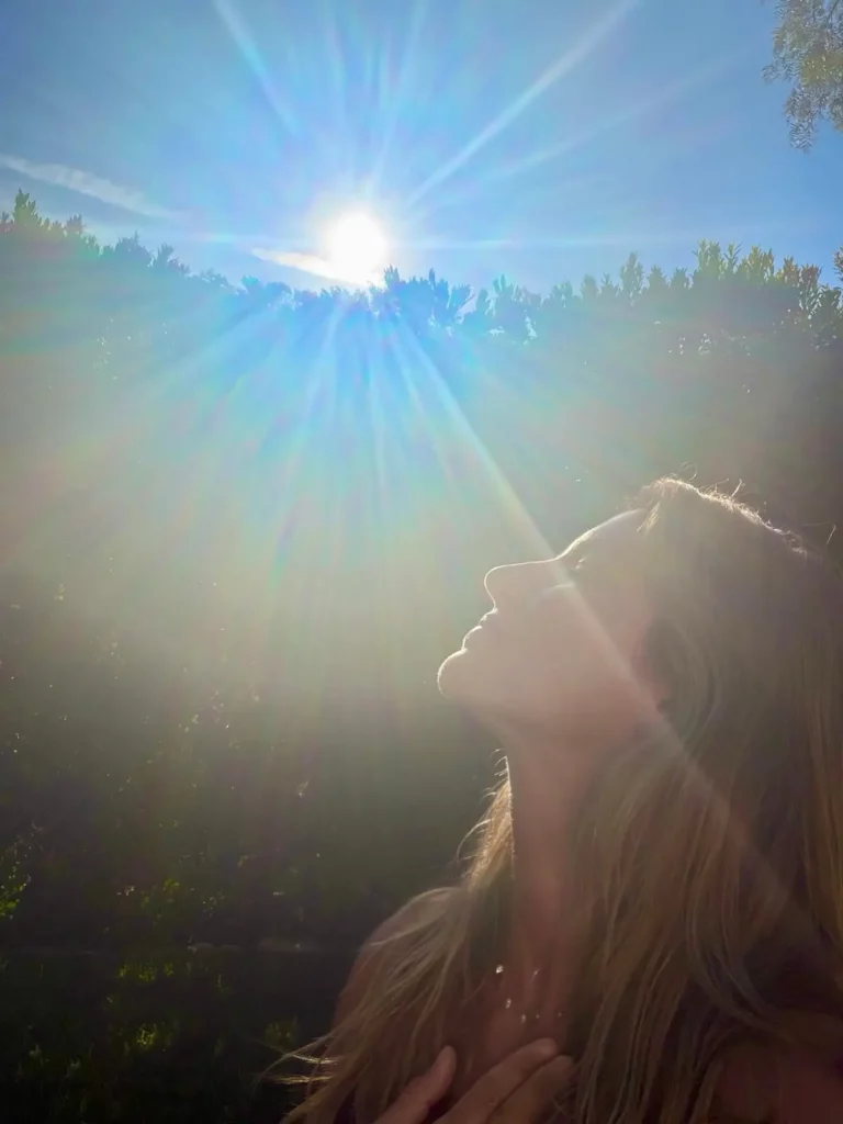Gisele Bündchen observa o céu ensolarado durante a celebração do aniversário em um jardim, em um momento de contemplação.